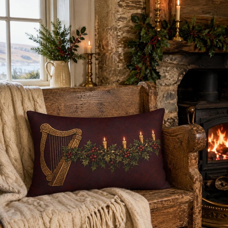 May include: A rectangular throw pillow in a deep burgundy color featuring a printed graphic of a golden Celtic harp and a festive garland of green holly leaves, red berries, and four lit taper candles arranged horizontally across the center.