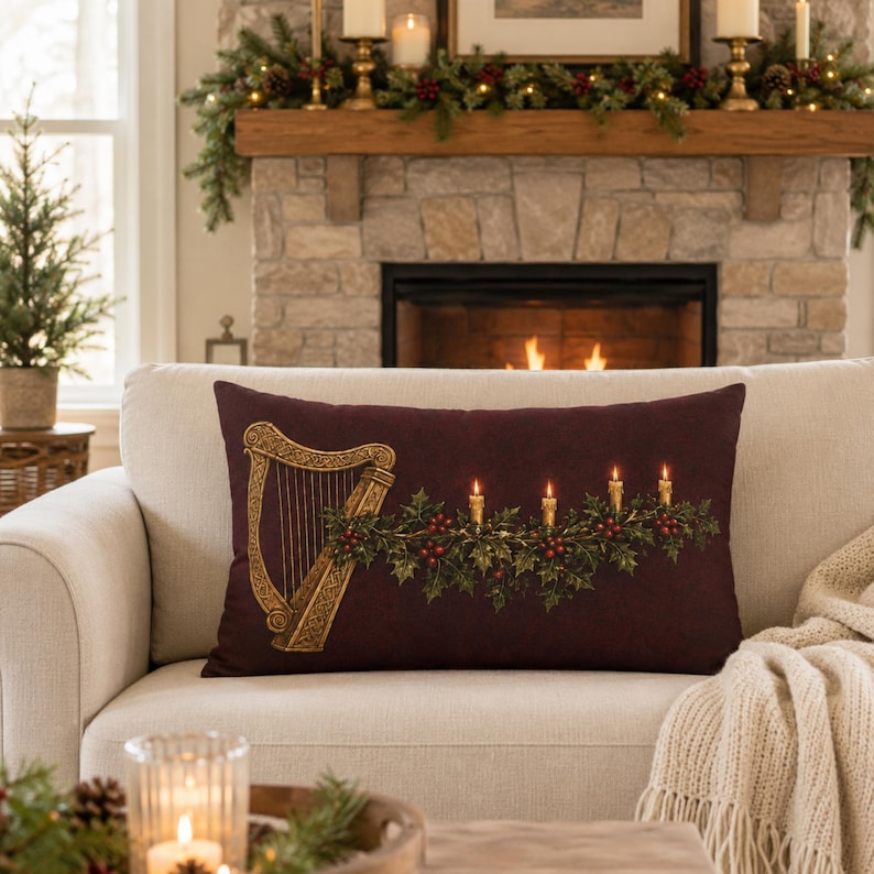 May include: A rectangular throw pillow in a deep burgundy color featuring a gold-toned harp on the left side and a horizontal garland of green holly leaves with red berries and four lit taper candles extending across the center and right side.