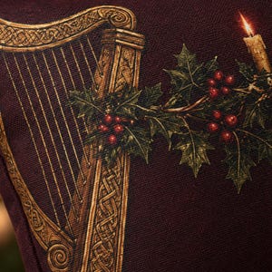 May include: A dark burgundy fabric cushion cover featuring a printed design of a golden Celtic harp. The illustration includes a sprig of green holly leaves with bright red berries and a single lit candle with a glowing flame on the right side.