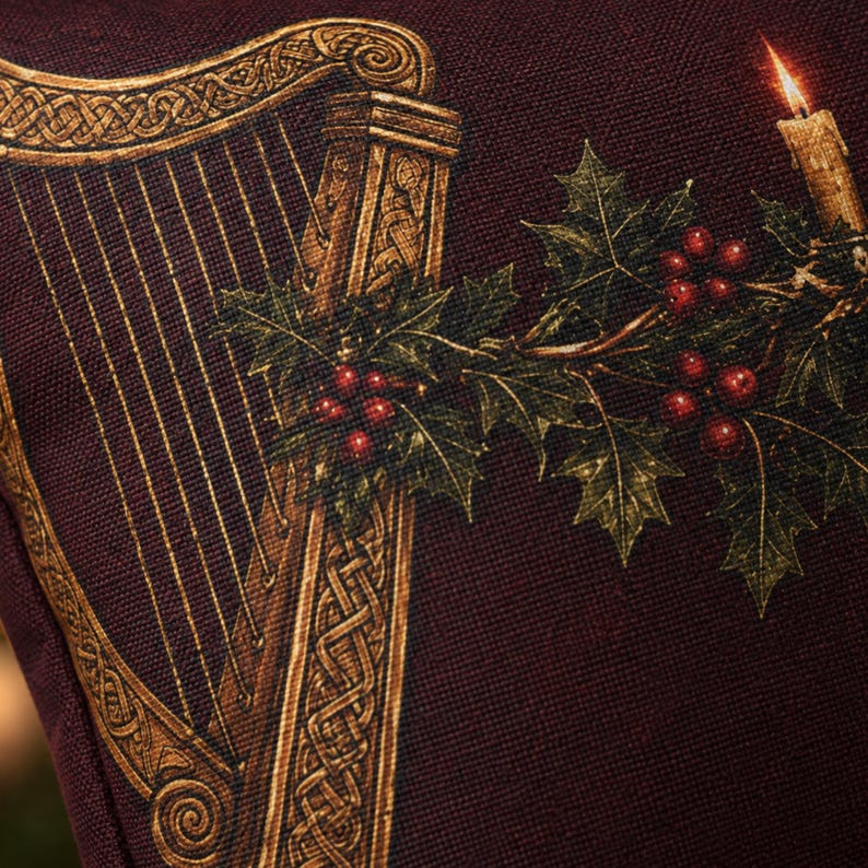 May include: A dark burgundy fabric cushion cover featuring a printed design of a golden Celtic harp. The illustration includes a sprig of green holly leaves with bright red berries and a single lit candle with a glowing flame on the right side.