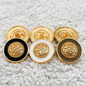 May include: A set of three round buttons featuring a gold-tone metal center with an intricate swirling filigree pattern. Each button has a distinct outer rim in black, white, or brown, with a gold-tone metal border and a shank back for attachment.
