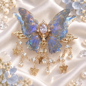 May include: A hair clip featuring a large, iridescent blue butterfly with gold-toned wing veins and a central oval crystal. The accessory includes dangling gold chains adorned with small crystal rhinestones and miniature gold butterfly charms.