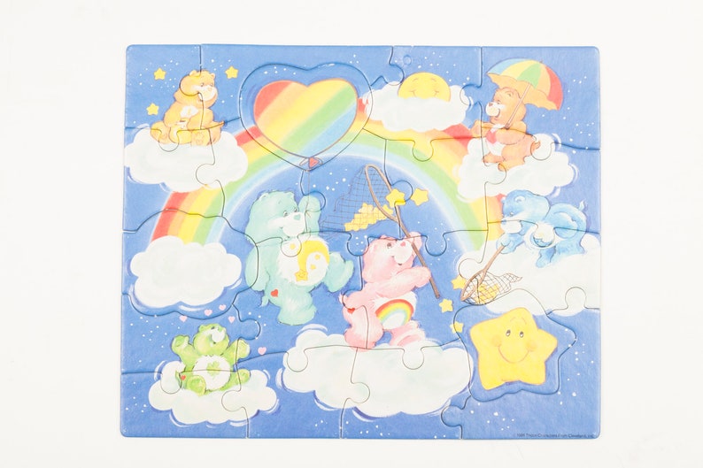 Może przedstawiać: Kolorowa układanka z Care Bears z tęczą, chmurami i gwiazdami. Care Bears bawią się siatką i balonem w kształcie serca.