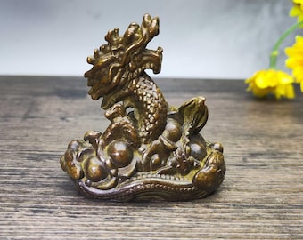 May include: A bronze-colored dragon figurine, intricately detailed with scales and a flowing mane. The dragon is posed atop a cloud-like base. The sculpture is displayed on a wooden surface.