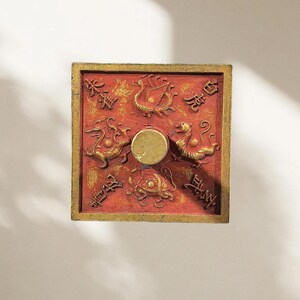 May include: A square red and gold decorative wall plaque featuring a central circular knob. The surface displays four embossed mythical creatures in gold, each accompanied by Chinese characters, arranged around the centre point.