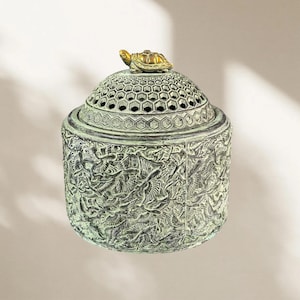 May include: A cylindrical incense burner with a weathered green finish featuring an intricate relief of flying birds on the body. The domed lid has a hexagonal honeycomb pattern and is topped with a small, gold-colored turtle figurine.