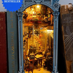 Könnte beinhalten: Ein Miniatur-Bücherregal-Einsatz mit einer detaillierten Bibliotheksszene, bestehend aus einem Schreibtisch, einer Schreibmaschine, Bücherregalen, einem Schiffssteuerrad und warmer Innenbeleuchtung, eingerahmt von einem verzierten blauen Torbogen.