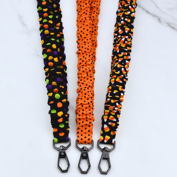 May include: Three fabric lanyards with metal swivel clasps. The left lanyard is black with purple, green, and orange polka dots. The center lanyard is orange with black polka dots. The right lanyard is black with a candy corn pattern.