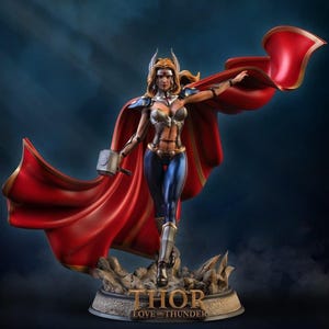 May include: A detailed statue of Thor from "Love and Thunder" stands on a rocky base. She wears a silver and blue armored outfit, a red cape, and holds a hammer. The statue has a dynamic pose with the text "THOR LOVE AND THUNDER" on the base.
