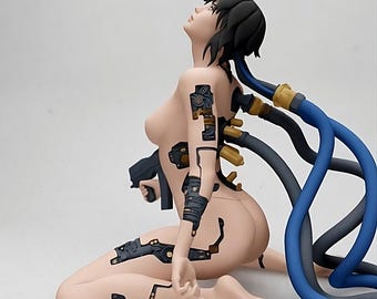 May include: A figurine of a seated figure with exposed mechanical components and black hair. The figure has blue and gray tubes connected to the back and is looking upwards. The figure is nude with mechanical parts.