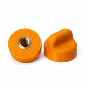 May include: Two orange cabinet knobs. One is a flat disc with a brass insert, and the other is a rounded shape with a handle. The knobs are made of a solid, matte material.