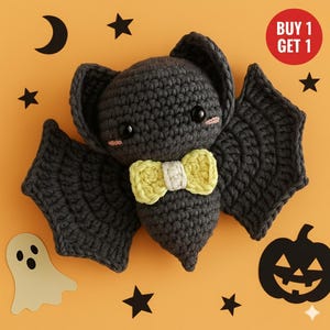 Pode incluir: Um morcego de crochê cinza escuro com uma gravata borboleta amarela e bochechas rosadas. O fundo laranja apresenta uma lua, estrelas, um fantasma e uma abóbora de Halloween. Um círculo vermelho diz "COMPRE 1 LEVE 1".
