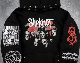 May include: A black hooded sweatshirt featuring a large Slipknot graphic with band members on the chest. The sleeves display a barcode with the text PEOPLE=SHIT, a nonagram symbol, a red tribal S logo, and a barbed wire graphic. Silver eyelets line the hood.