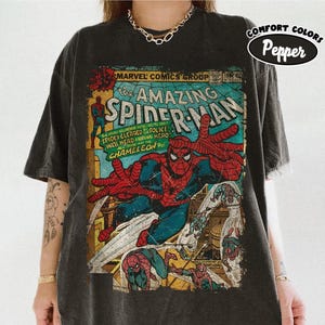 May include: Dark gray t-shirt featuring a vintage comic book cover of Spider-Man. The graphic includes the text "The Amazing Spider-Man" and "Marvel Comics Group." The shirt is from Comfort Colors.