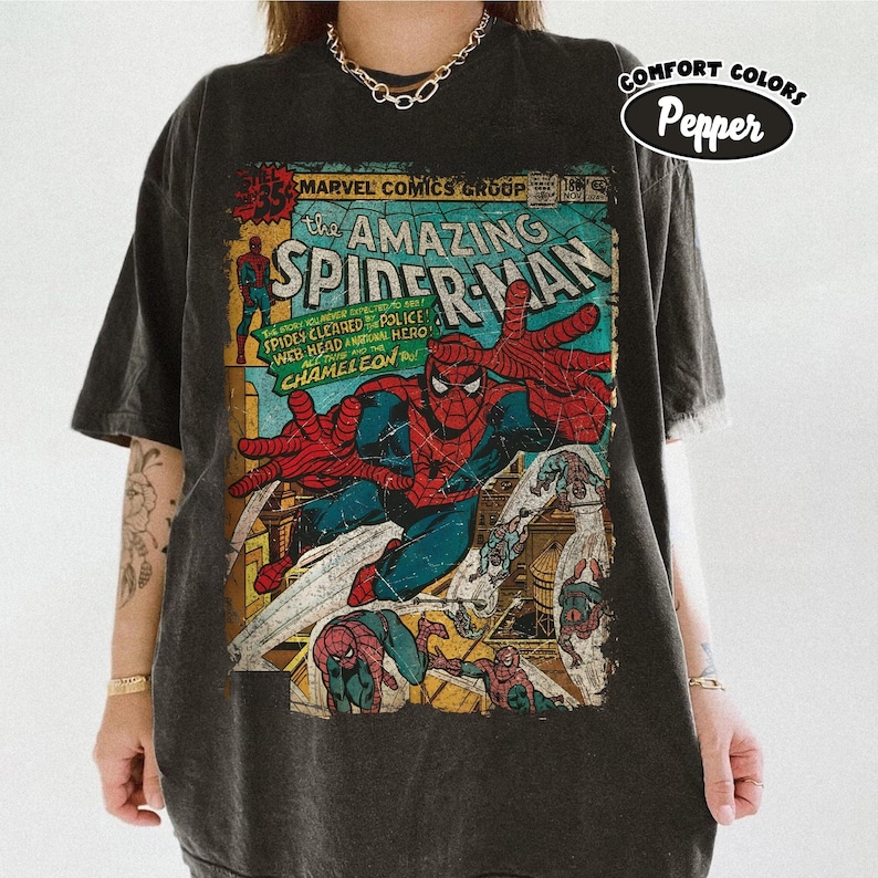 May include: Dark gray t-shirt featuring a vintage comic book cover of Spider-Man. The graphic includes the text "The Amazing Spider-Man" and "Marvel Comics Group." The shirt is from Comfort Colors.