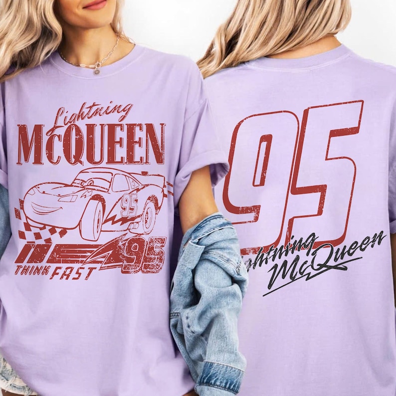 May include: Pale purple t-shirt with a red graphic of Lightning McQueen and the number 95. The front of the shirt displays the text "Lightning McQueen" and "Think Fast". The back of the shirt has a large "95" and "Lightning McQueen".