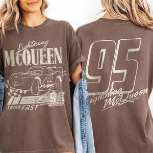 May include: Brown t-shirt with a Lightning McQueen design. The front shows the character, the number 95, and the words "THINK FAST." The back of the shirt has a large "95" and the text "Lightning McQueen".