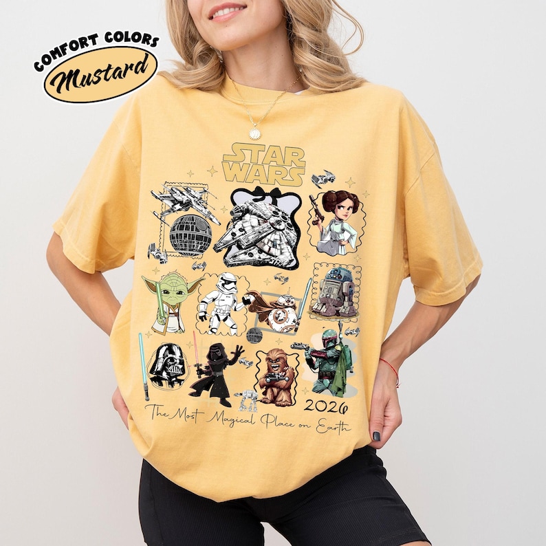 K&ouml;nnte beinhalten: Senffarbenes T-Shirt mit einem Star Wars-Motiv, das verschiedene Charaktere und den Text "The Most Magical Place on Earth 2026" zeigt. Das Shirt hat auch die W&ouml;rter "Comfort Colors" und "Mustard" in einem Kreis.
