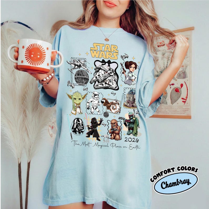 K&ouml;nnte beinhalten: Hellblaues T-Shirt mit Star Wars-Charakteren und dem Text "Star Wars 2026 The Most Magical Place on Earth." Das Shirt hat auch das Comfort Colors Chambray-Logo und eine Tasse mit einem Sonnendesign.