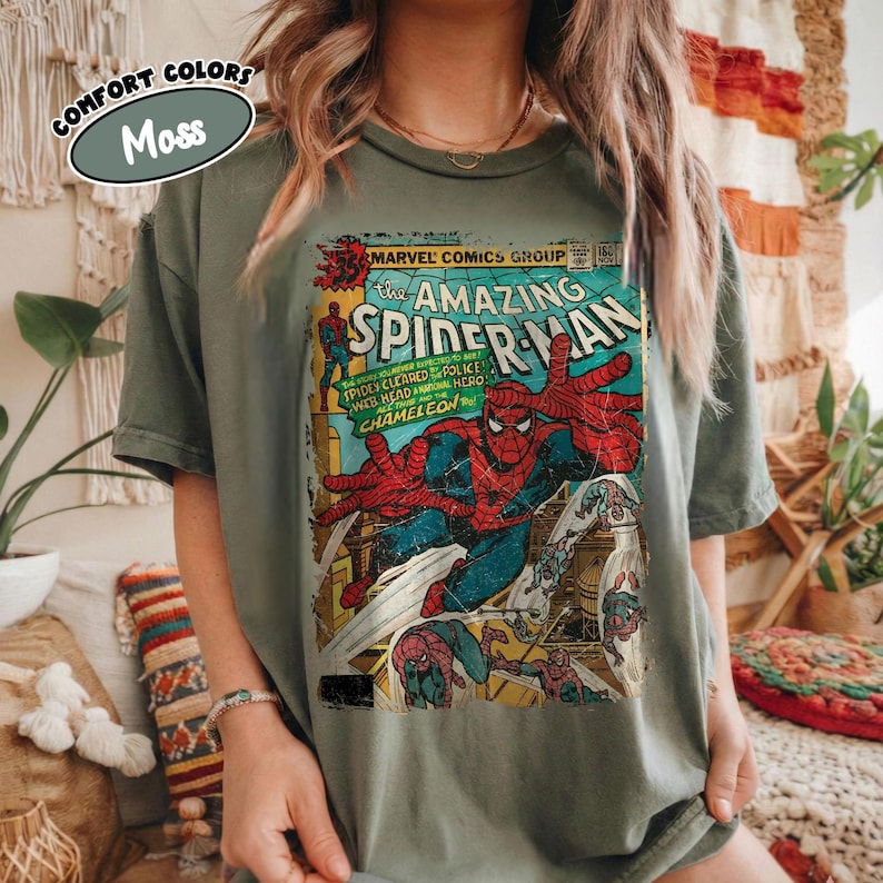 May include: A moss green t-shirt featuring a vintage comic book cover of The Amazing Spider-Man. The comic art shows Spider-Man in action with red and blue colors. The shirt has the text "COMFORT COLORS" and "Moss" on it.
