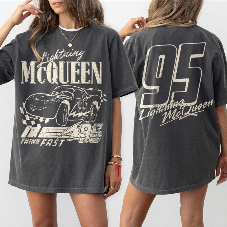 May include: Dark grey t-shirt featuring Lightning McQueen from the film Cars. The front graphic includes the character, the number 95, and the words "Lightning McQueen" and "Think Fast." The back of the shirt displays a large number 95 and the words "Lightning McQueen."