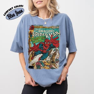 May include: Blue jean colored t-shirt featuring a vintage comic book cover of The Amazing Spider-Man. The comic book cover has a distressed look with Spider-Man in action, with the text "MARVEL COMICS GROUP" and "SPIDER-MAN".