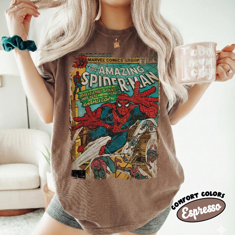 May include: Brown t-shirt featuring a vintage comic book cover of The Amazing Spider-Man. The comic art shows Spider-Man in action with vibrant red, blue, and yellow colors. The shirt has the text "MARVEL COMICS GROUP" and "COMFORT COLORS Espresso".