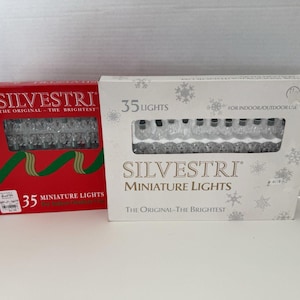 May include: Two rectangular boxes of Silvestri miniature lights. The left box is red with a green ribbon graphic, while the right box is white with snowflake patterns. Each box contains 35 clear miniature lights for indoor or outdoor use.