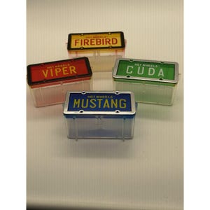 May include: Four rectangular Hot Wheels storage containers with translucent bodies in yellow, red, green, and blue. Each lid features a metallic-look frame resembling a license plate with the text FIREBIRD, VIPER, CUDA, or MUSTANG printed on it.