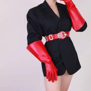 May include: A black blazer, red gloves, and a red belt with a rhinestone buckle. The gloves extend past the elbows. The belt is worn at the waist, creating a defined silhouette.