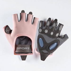 Puede incluir: Un par de guantes de entrenamiento sin dedos. Los guantes son rosas con detalles negros y una palma de malla gris. La palabra "SPORT" está impresa en una etiqueta en la muñeca. Diseñados para actividades de fitness.