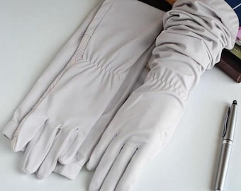 May include: A pair of light gray, long-sleeved gloves with a mesh detail on the upper arm. The gloves are made of a smooth material and are designed to cover the hands and forearms. A silver pen rests beside the gloves.