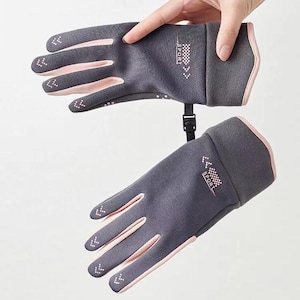 May include: Gray and pink sport gloves with the word "SPORT" printed on the wrist. The gloves have a pink trim and a black adjustable strap. The fingertips have small white arrow designs.
