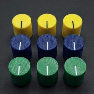 Puede incluir: Nueve perillas cil&iacute;ndricas en una cuadr&iacute;cula de 3x3. La fila superior es amarilla, la fila del medio es azul y la fila inferior es verde. Cada perilla tiene una l&iacute;nea vertical blanca en la parte superior. Las perillas est&aacute;n sobre una superficie oscura.