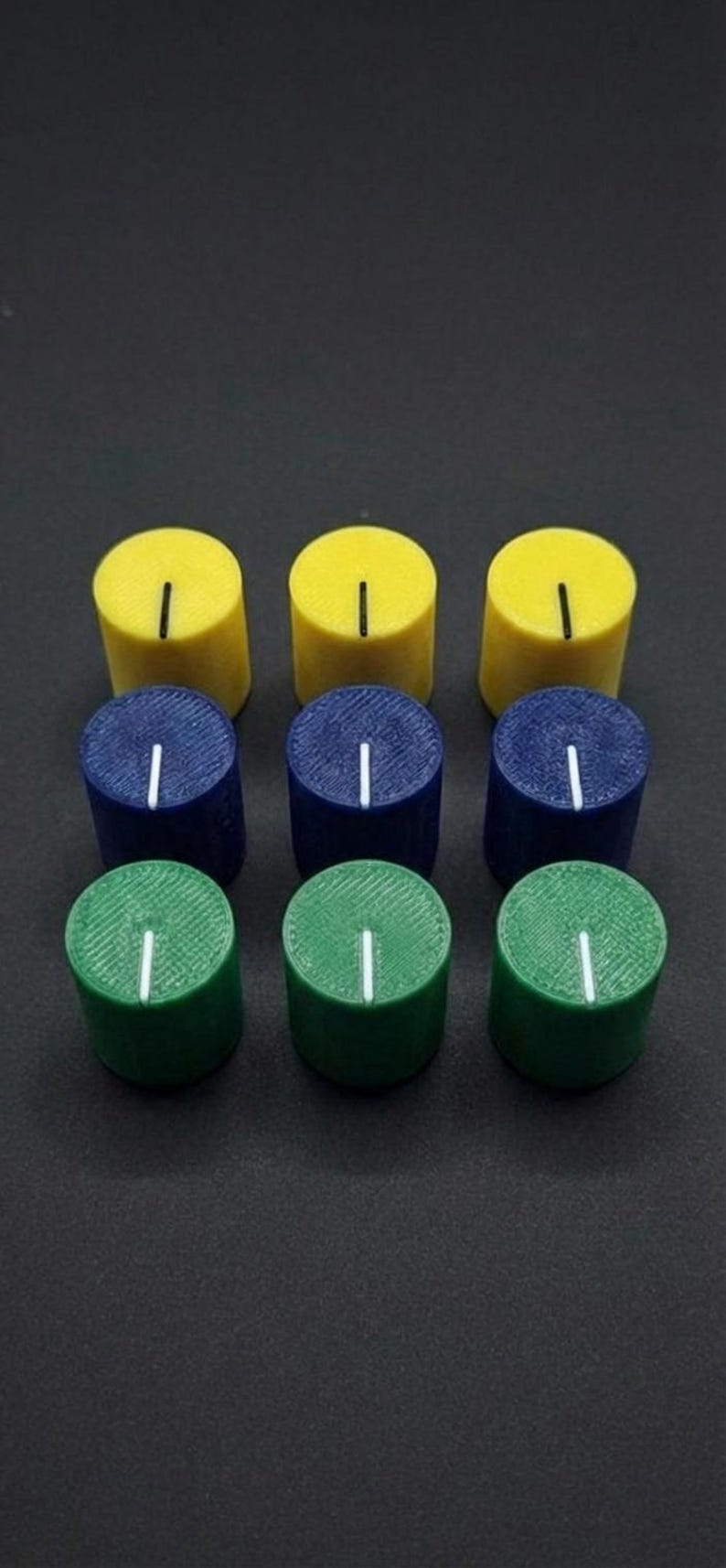 Puede incluir: Nueve perillas cil&iacute;ndricas en una cuadr&iacute;cula de 3x3. La fila superior es amarilla, la fila del medio es azul y la fila inferior es verde. Cada perilla tiene una l&iacute;nea vertical blanca en la parte superior. Las perillas est&aacute;n sobre una superficie oscura.