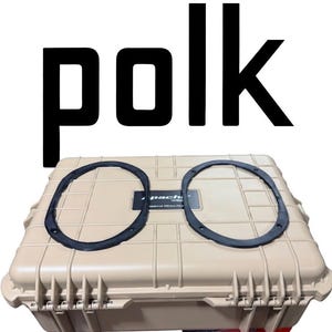 May include: Tan case with two black speaker rings and the word "polk" in large black letters above. The case has a rectangular shape with a ridged surface and a black label.