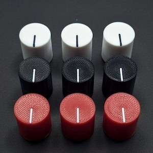 May include: Nine cylindrical control knobs in three colors: white, black, and red. Each knob has a white vertical line indicator. The knobs are arranged in a 3x3 grid against a dark background.