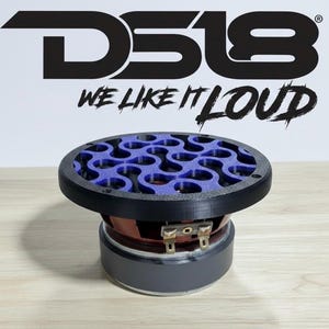 Puede incluir: Un altavoz con marco negro y rejilla con diseño azul. El altavoz tiene una base gris oscuro y un cono marrón. El texto "DS18 WE LIKE IT LOUD" está encima del altavoz en negro.