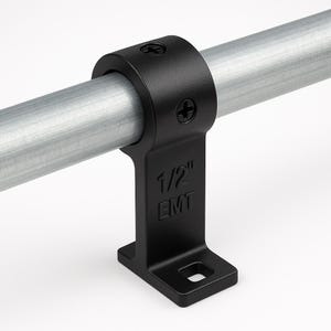 May include: A black 1/2" EMT conduit clamp securing a silver metal pipe. The clamp has a rounded top with two screws and a rectangular base with a mounting hole. The text "1/2" EMT" is visible on the clamp.