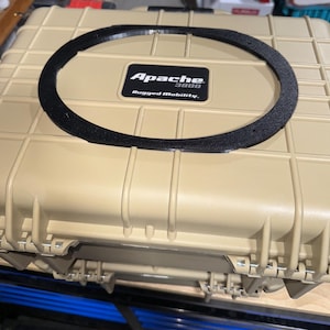 以下が含まれることがあります： 黒いガスケットが付いた、タン色のApache 3800頑丈なモビリティケース。ケースは長方形で、上部に格子模様があります。Apacheのロゴとテキストが前面に表示されています。