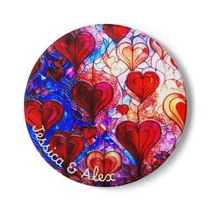 Peut inclure: Objet décoratif rond avec un motif de cœur en vitrail rouge, bleu et blanc. Les noms "Jessica & Alex" sont écrits en cursive en bas à gauche.