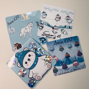 May include: Four square stickers with winter designs. One shows a polar bear in a blue hat and scarf with holographic details. Other stickers feature a wolf, penguins, and winter hats. Text includes "Save £20" and "Each icon = £2".