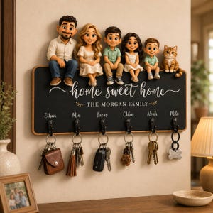 Pode incluir: Um porta-chaves de parede retangular preto com moldura de madeira e seis ganchos metálicos. A placa exibe o texto "home sweet home" e "THE MORGAN FAMILY" acima dos nomes Ethan, Mia, Lucas, Chloe, Noah e Milo. Seis figuras de estilo cartoon de quatro crianças, dois adultos e um gato estão sentadas na borda superior. Várias chaves e porta-chaves estão pendurados nos ganchos.