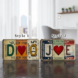 May include: Two decorative signs spelling "DOE" and "JOE" using vintage license plates. The "DOE" sign features a red heart and the letters "D" and "E". The "JOE" sign also has a red heart and the letters "J" and "E".