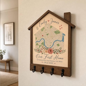 May include: A house-shaped wooden wall-mounted key holder featuring a printed map with a blue river, floral accents, and the text Emily and James, Our First Home, 123 Greencircle St, San Francisco, CA, 98765, and 04.12.2024 with four black metal hooks.