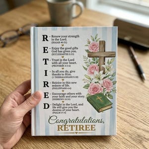 May include: A hardcover book with a floral and cross design. The cover features the word "RETIRED" spelled out with inspirational messages. The words "Congratulations, RETIREE" are at the bottom. The book is held by a person.