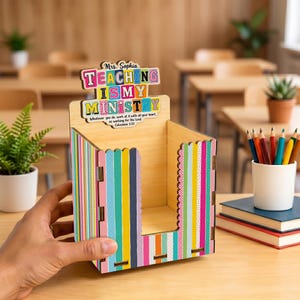 Könnte beinhalten: Ein Schreibtisch-Organizer aus Holz mit vertikalen Streifen in Pink, Gelb, Blau und Orange. Das Schild oben trägt die Aufschrift "Mrs. Sophia TEACHING IS MY MINISTRY" mit "Whatever you do, work at it with all your heart, as working for the Lord. Colossians 3:23".
