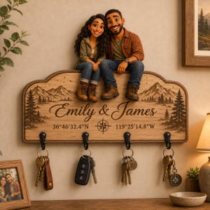 May include: A wooden wall-mounted key holder featuring a laser-engraved mountain and forest landscape. The text reads Emily & James with coordinates 36°46'32.4"N 119°25'14.8"W. Two 3D figures sit on top. Four black metal hooks hold various sets of keys.