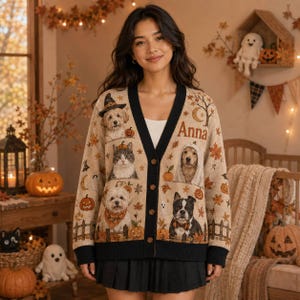May include: A beige V-neck cardigan featuring a black button placket and hem. The knit fabric displays a Halloween-themed pattern with various dog and cat illustrations, pumpkins, autumn leaves, and the name Anna printed on the right chest area.