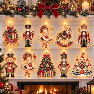 Op de afbeelding: Een set van tien verlichte kerstornamenten met een slee met cadeaus, notenkrakers, een ballerina, een hobbelpaard, een teddybeer met een trommel, een versierde kerstboom en een kasteel, gerangschikt in twee rijen tegen een witte open haard.